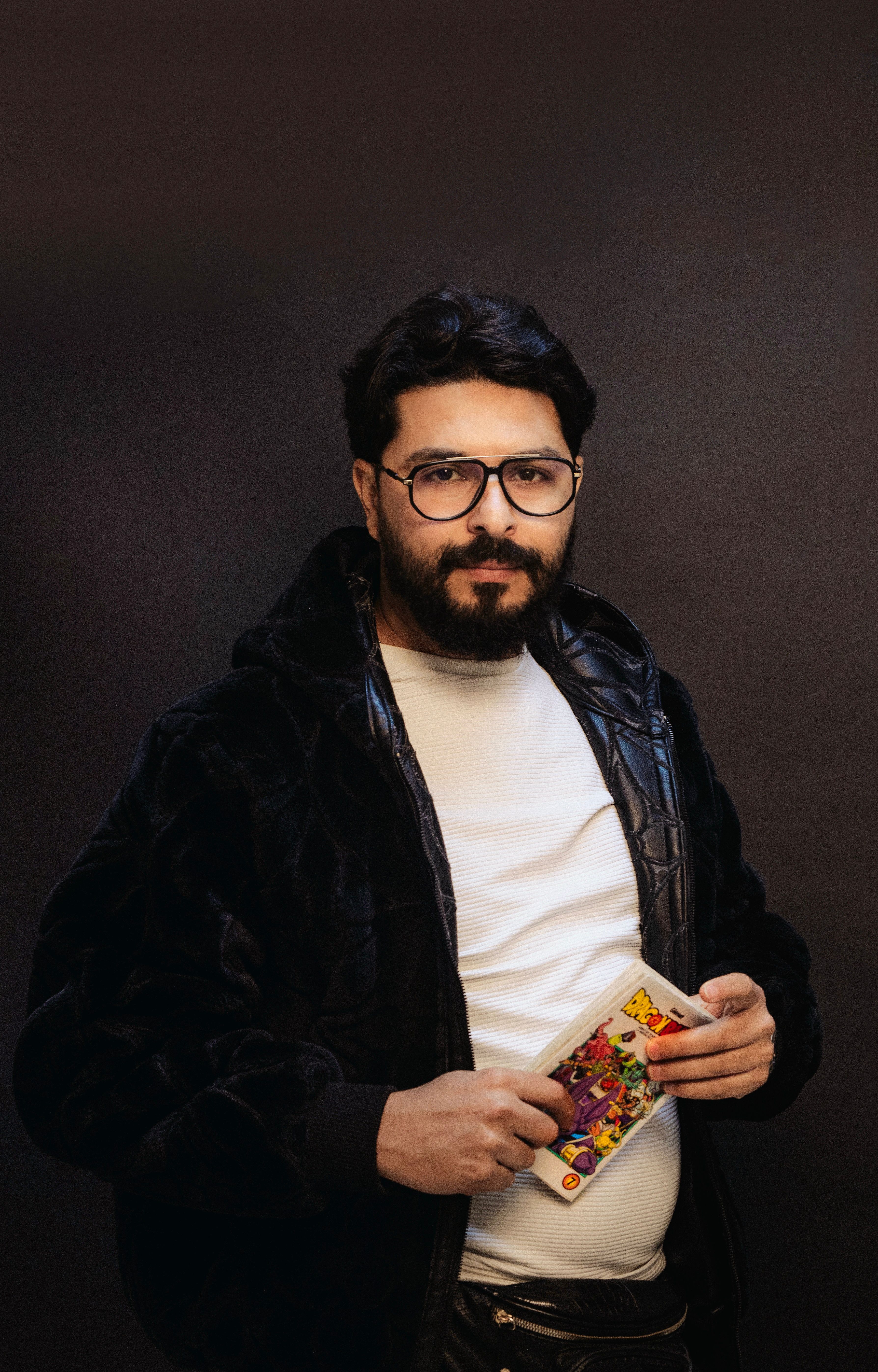 Studio portrait of a man with beard and glasses holding a colorful comic book.