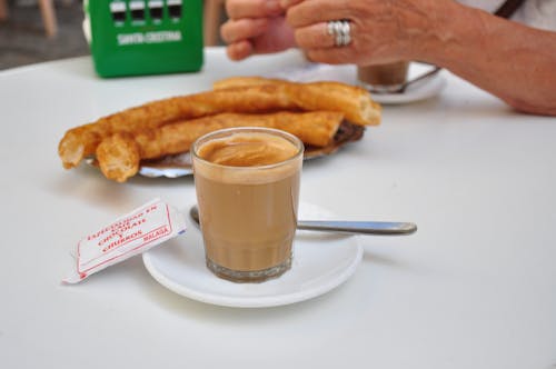 Coffee with milk in a glass with a plate of churros in the background