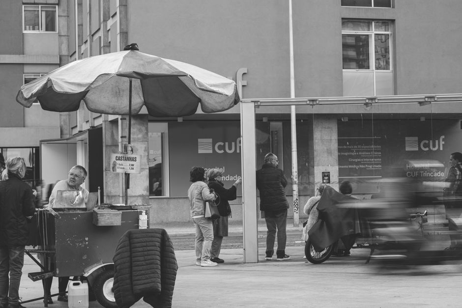 Black and white photo capturing a busy city street with a small food stall and pedestrians.