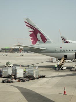 Qatar Airways aircraft parked at airport terminal with cargo being loaded on a sunny day.