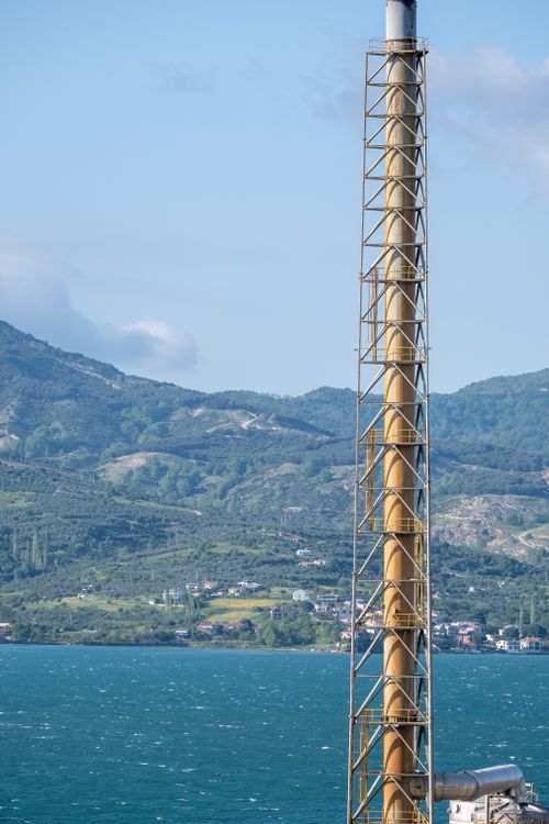 Free Vertical shot of an industrial chimney against mountains by the blue sea. Stock Photo