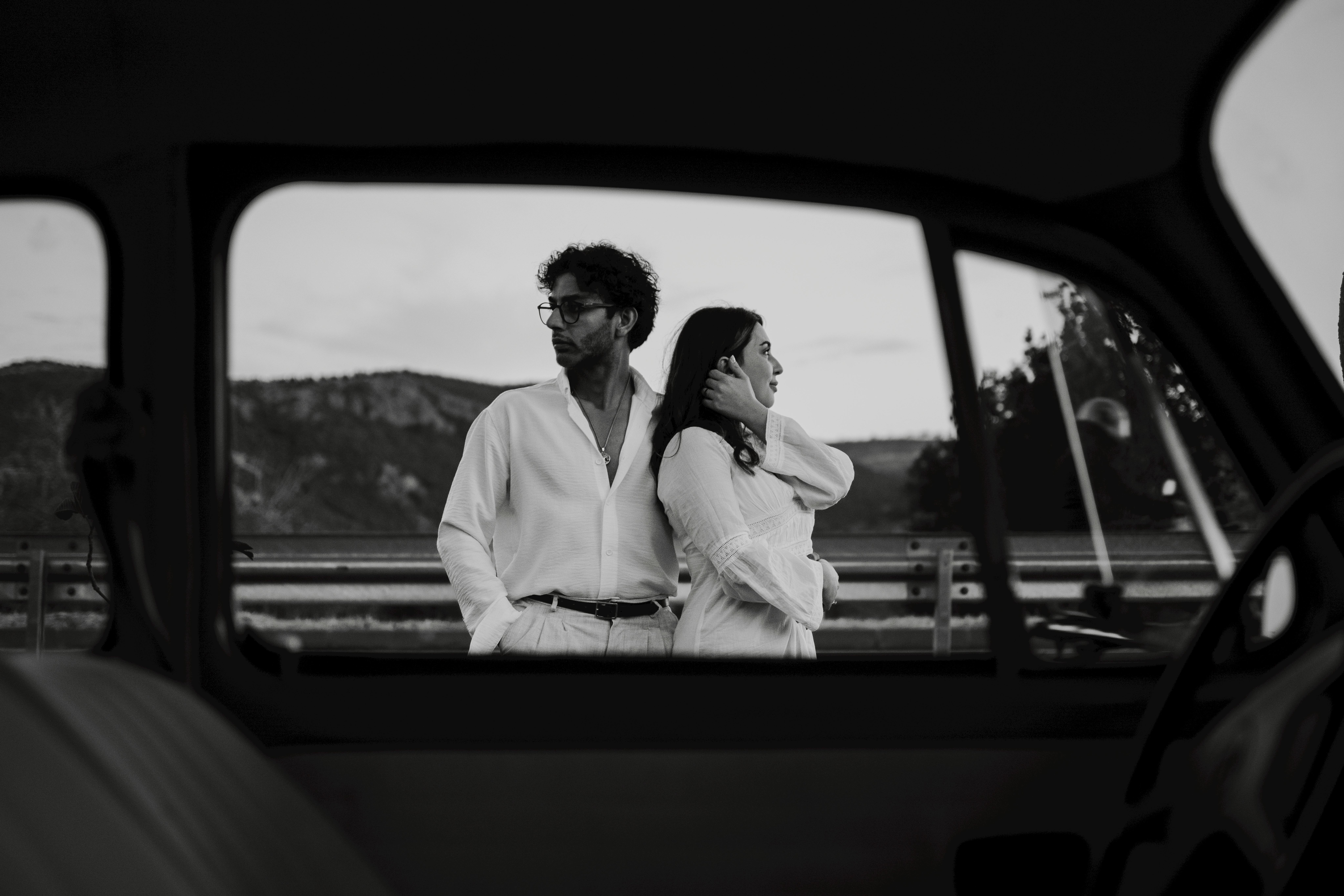 Artistic black and white photo of a stylish couple framed through a car window. Timeless fashion vibe.