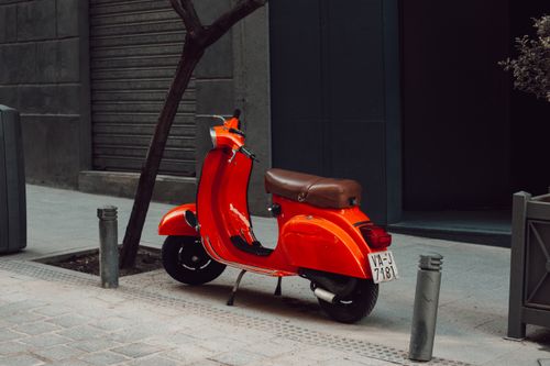 Free Vibrant red scooter parked on a sidewalk in Madrid, Spain. Urban city scene perfect for travel imagery. Stock Photo