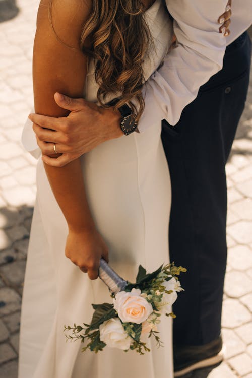 A bride and groom embrace in front of a brick wall