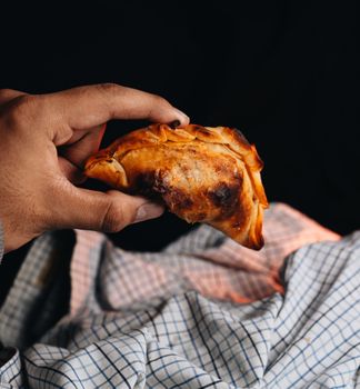 Close-up of a hand holding a freshly baked Argentine empanada with a cloth background.