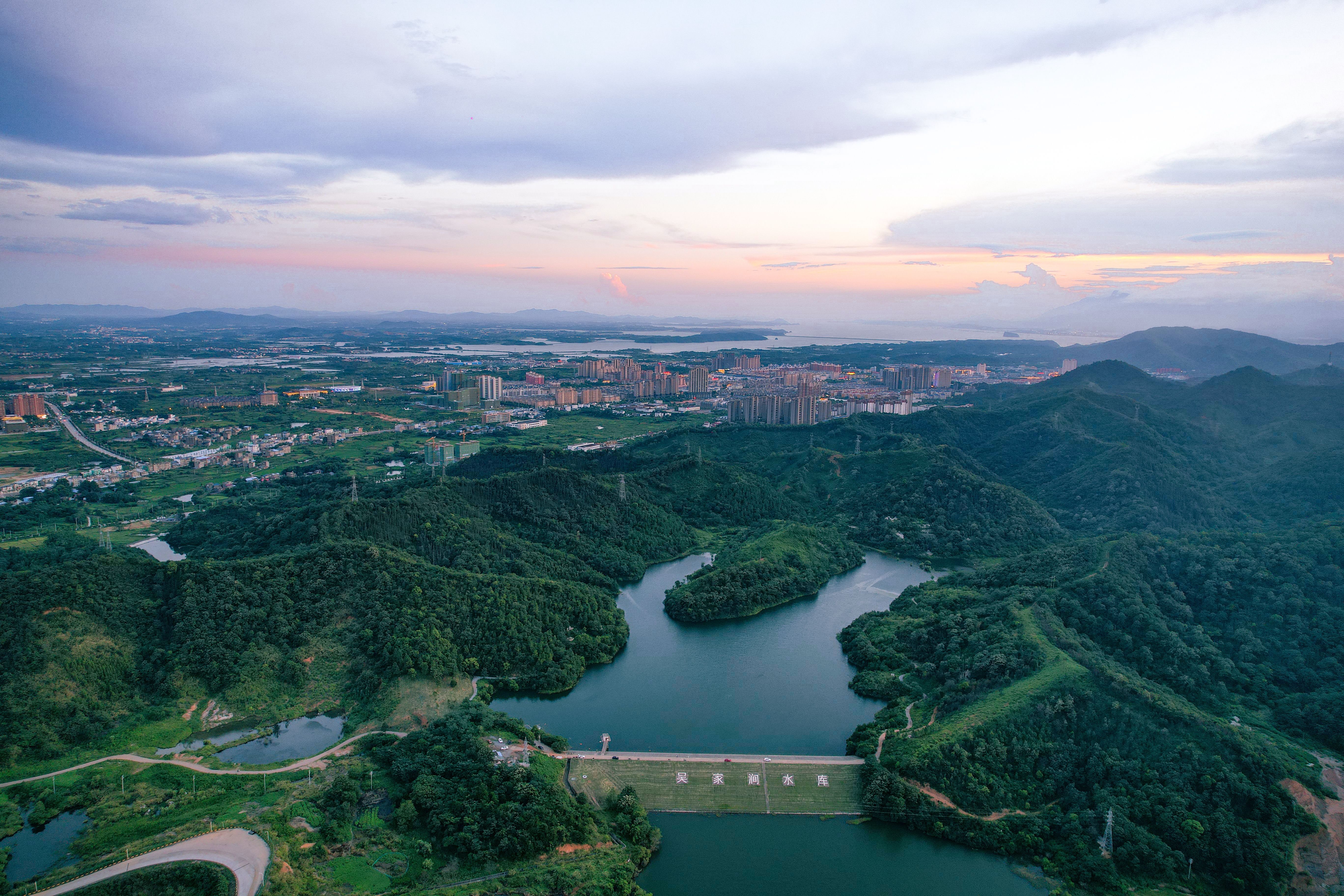 Beautiful aerial view of Jiujiang city and surrounding forests at sunset, showcasing lush green landscapes and serene lake.