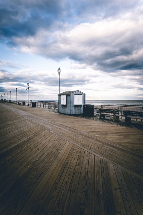 Free Tranquil seaside boardwalk view showcasing benches, a shed, and expansive ocean under a dramatic sky. Stock Photo