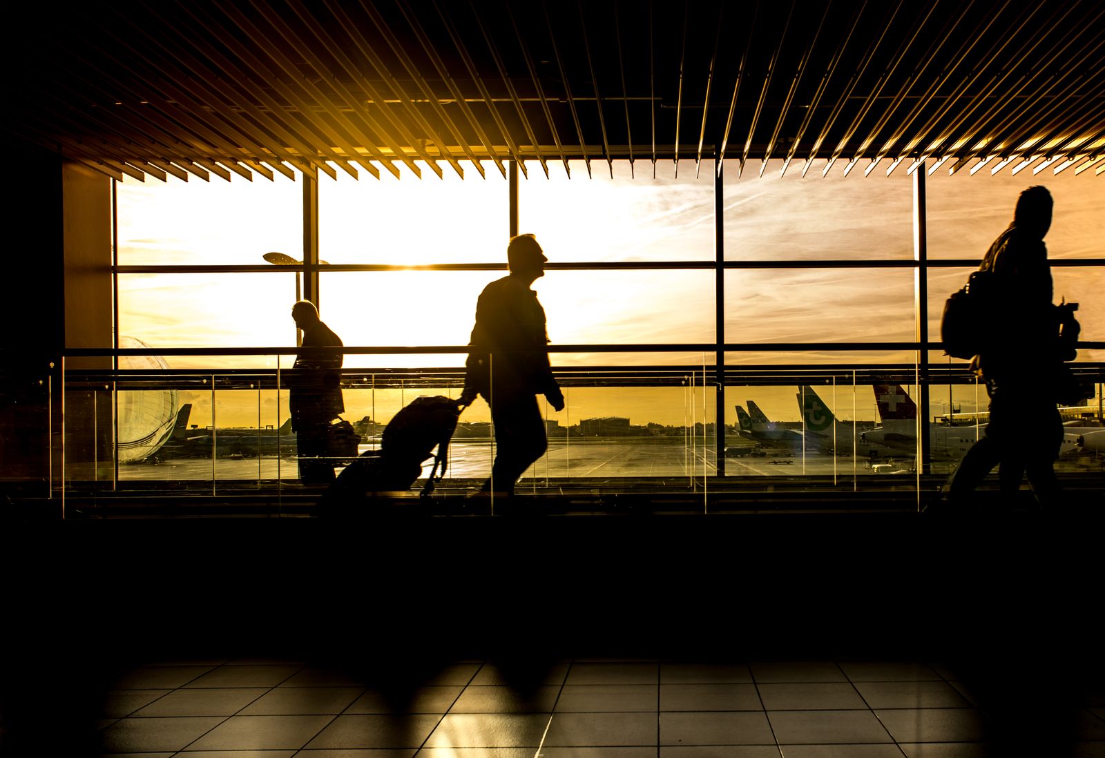 Travellers with luggage crossing an airport concourse at sunset.