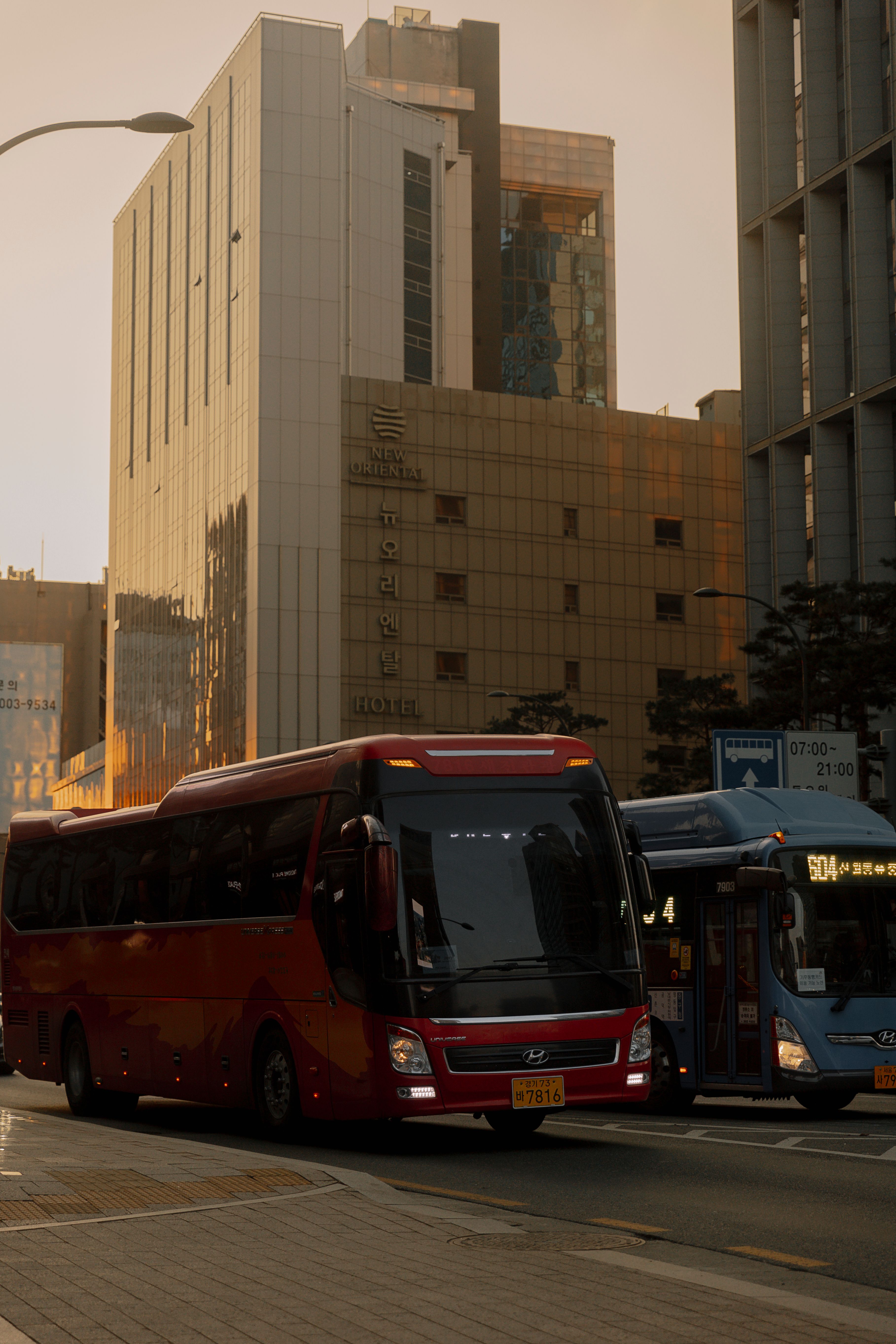 Busy urban street with red and blue buses amidst downtown buildings during daytime.
