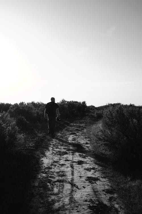 Monochrome Photo of Person Walking On Dirt Road