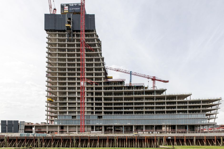 A futuristic skyscraper under construction with cranes in an urban setting.