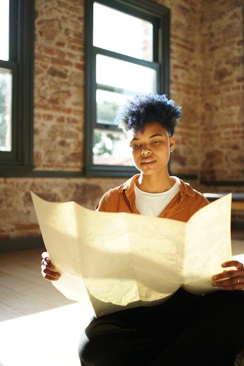 Free A thoughtful young woman examines a map in a sunlit room with brick walls. Stock Photo