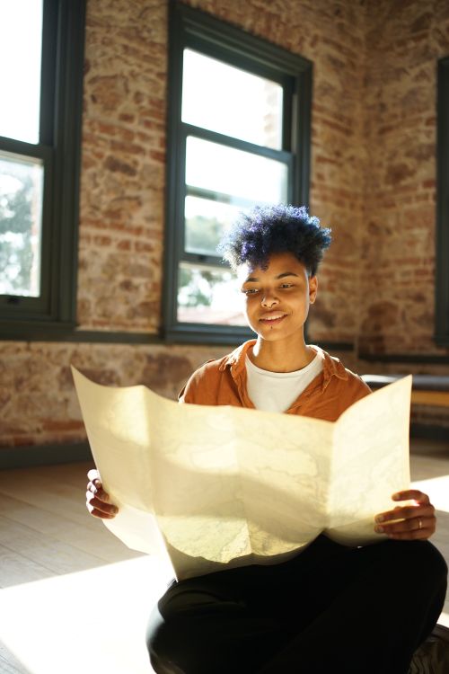 Free A cheerful woman sits indoors enjoying a map, exuding curiosity and warmth. Stock Photo