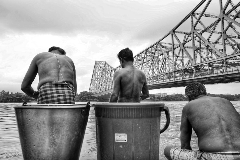 Black and white photo of men by the Howrah Bridge in Kolkata, India. Black and white photo of men by the Howrah Bridge in Kolkata, India.