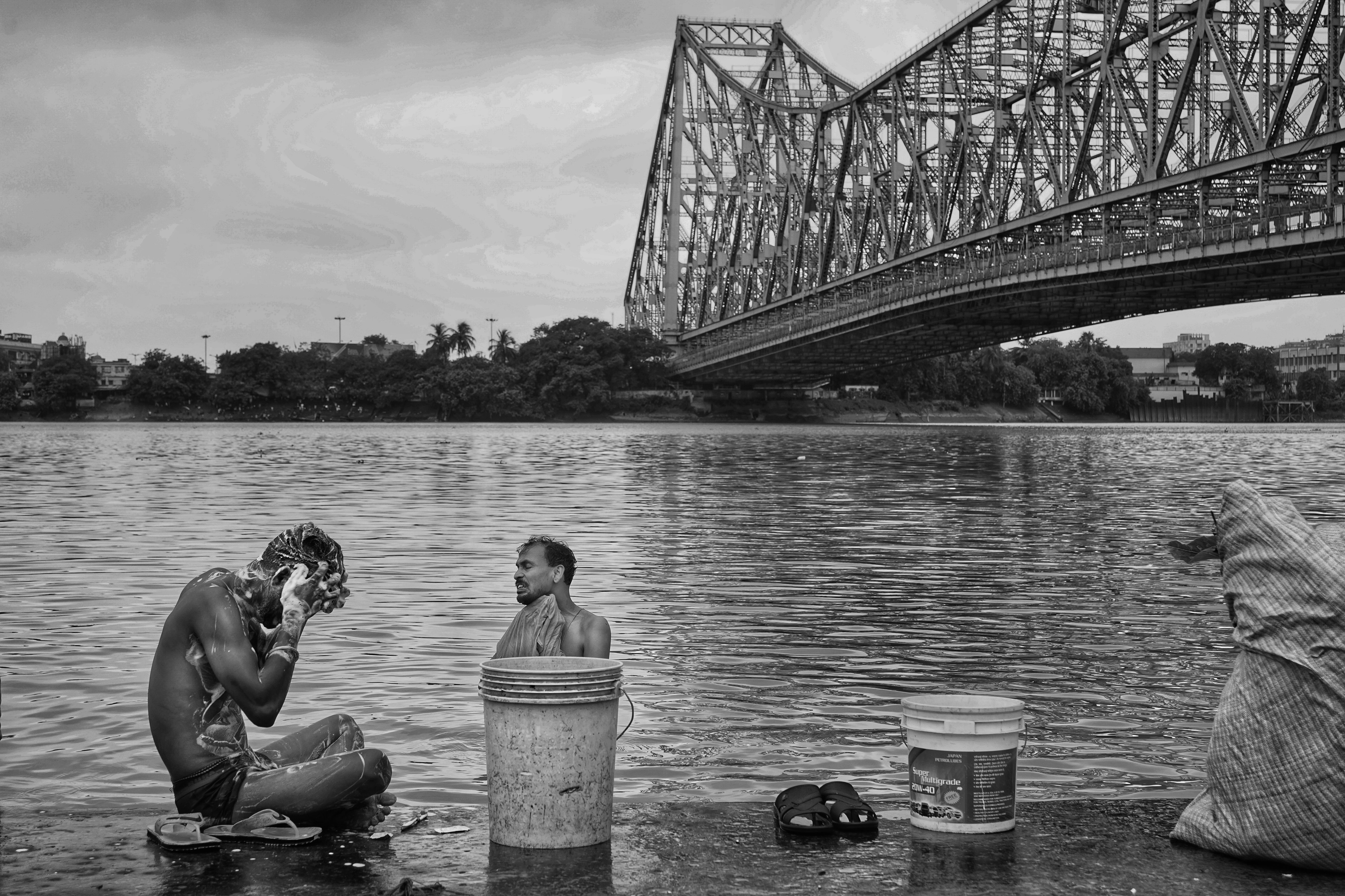 Two men wash in the Hooghly River beneath Kolkata's iconic Howrah Bridge.