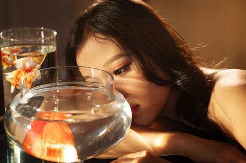 A woman is looking at a fish bowl with a glass of water