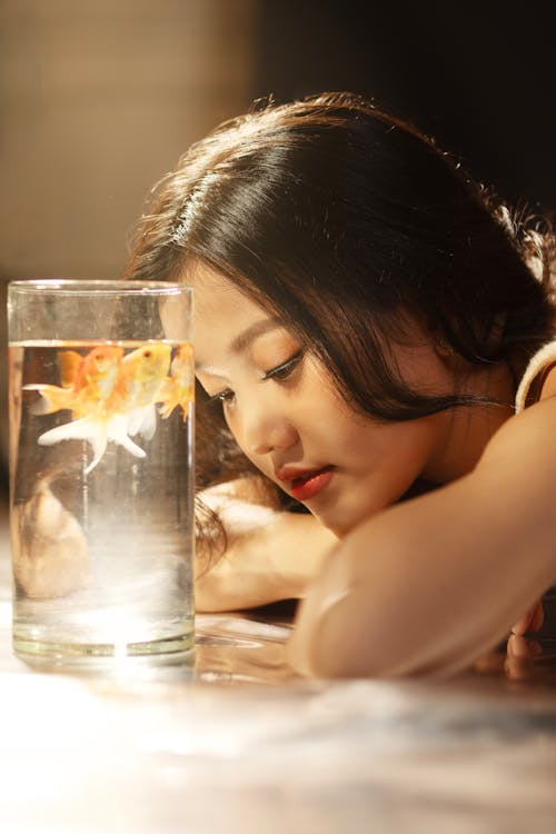 A woman is looking at a fish in a glass