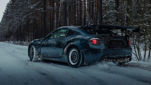Free Race car speeds through the snow-covered forest road during winter. Stock Photo