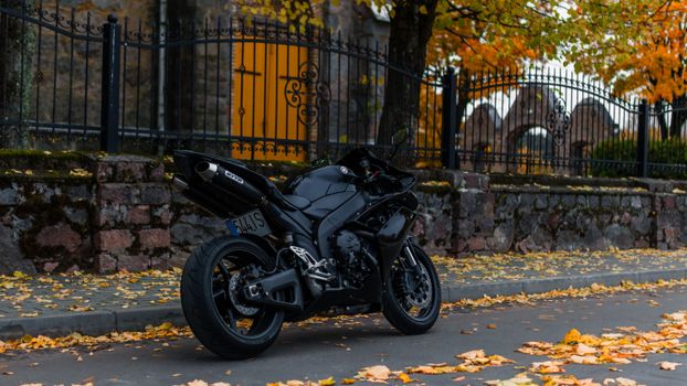 Black motorcycle parked on urban street with fall leaves and iron fence background.