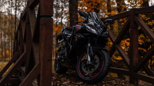 Free A sleek black motorcycle parked on a wooden footbridge surrounded by autumn foliage. Stock Photo