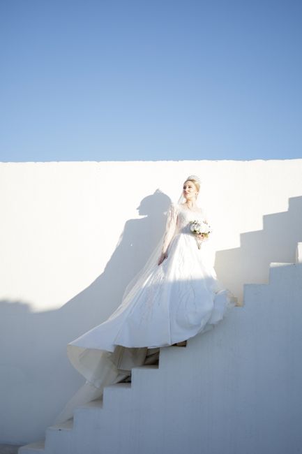 Bride in wedding dress on stairs against a clear blue sky, showcasing elegance and grace.