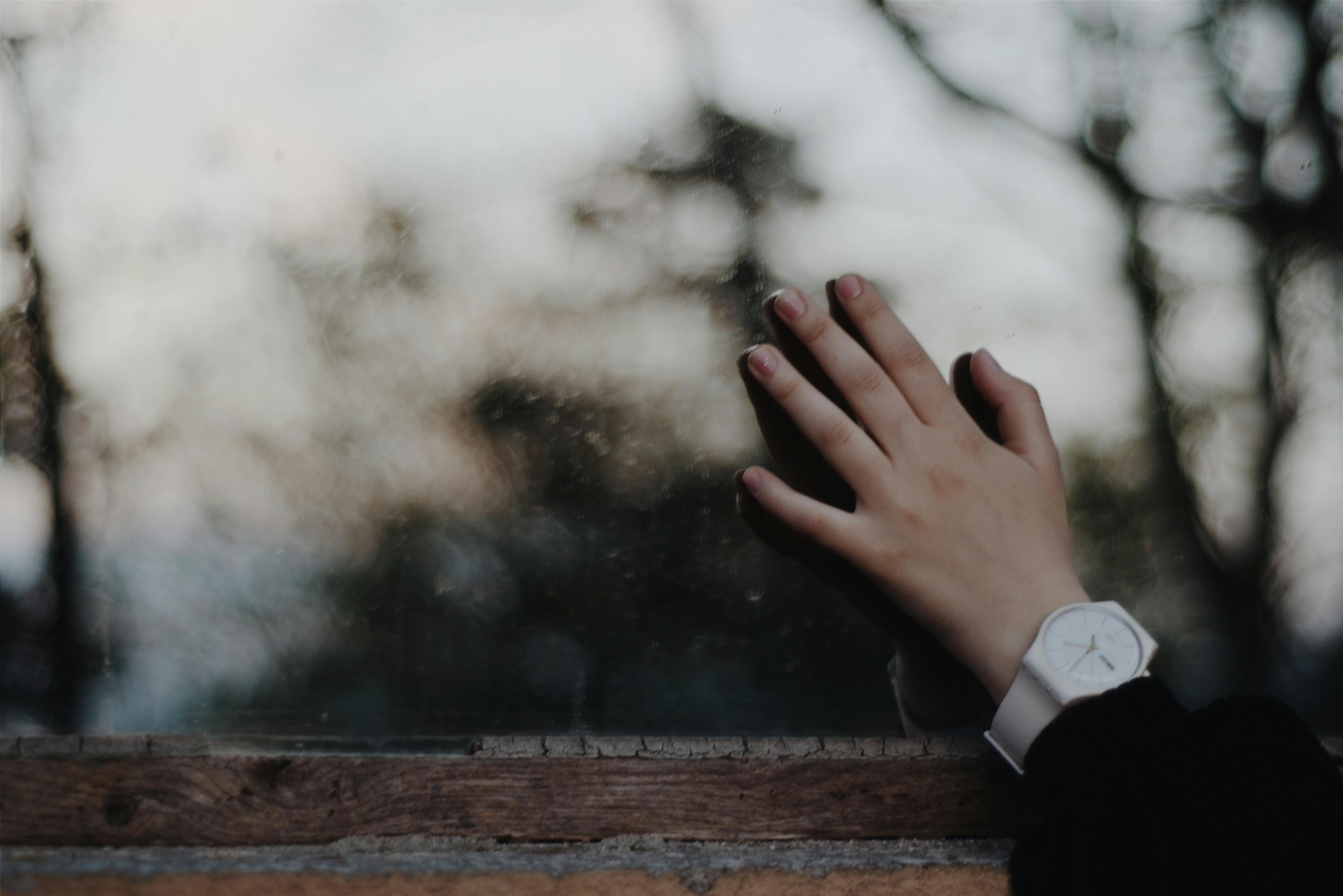 特写镜头中，一只戴着白色手表的手触摸着户外背景模糊的窗户