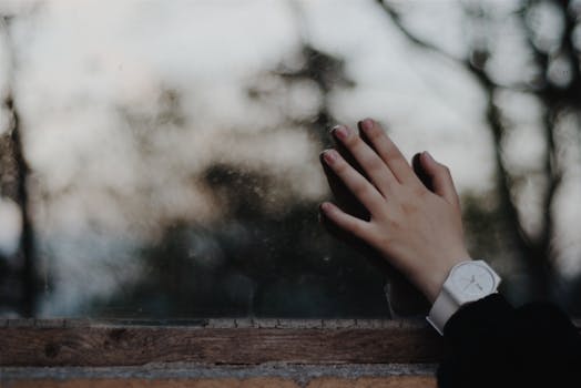 特写镜头中，一只戴着白色手表的手触摸着户外背景模糊的窗户