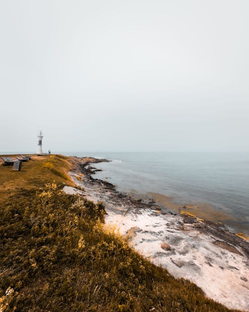 A lighthouse on a rocky shore with a foggy sky