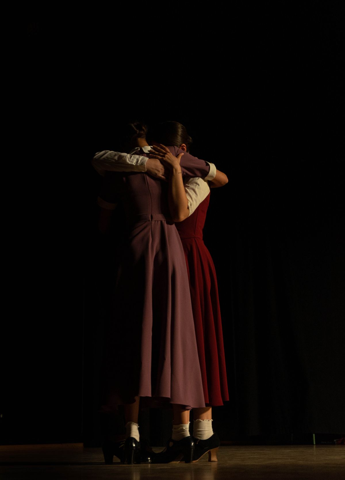 Two dancers in vintage dresses on a dark stage