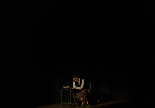 A dramatic studio portrait of a woman sitting at a table, deep in thought.