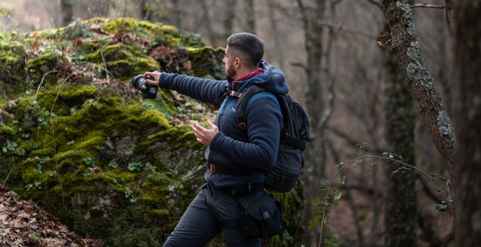 Man stands in a mossy forest capturing nature with camera. Adventurous outdoor photography scene.