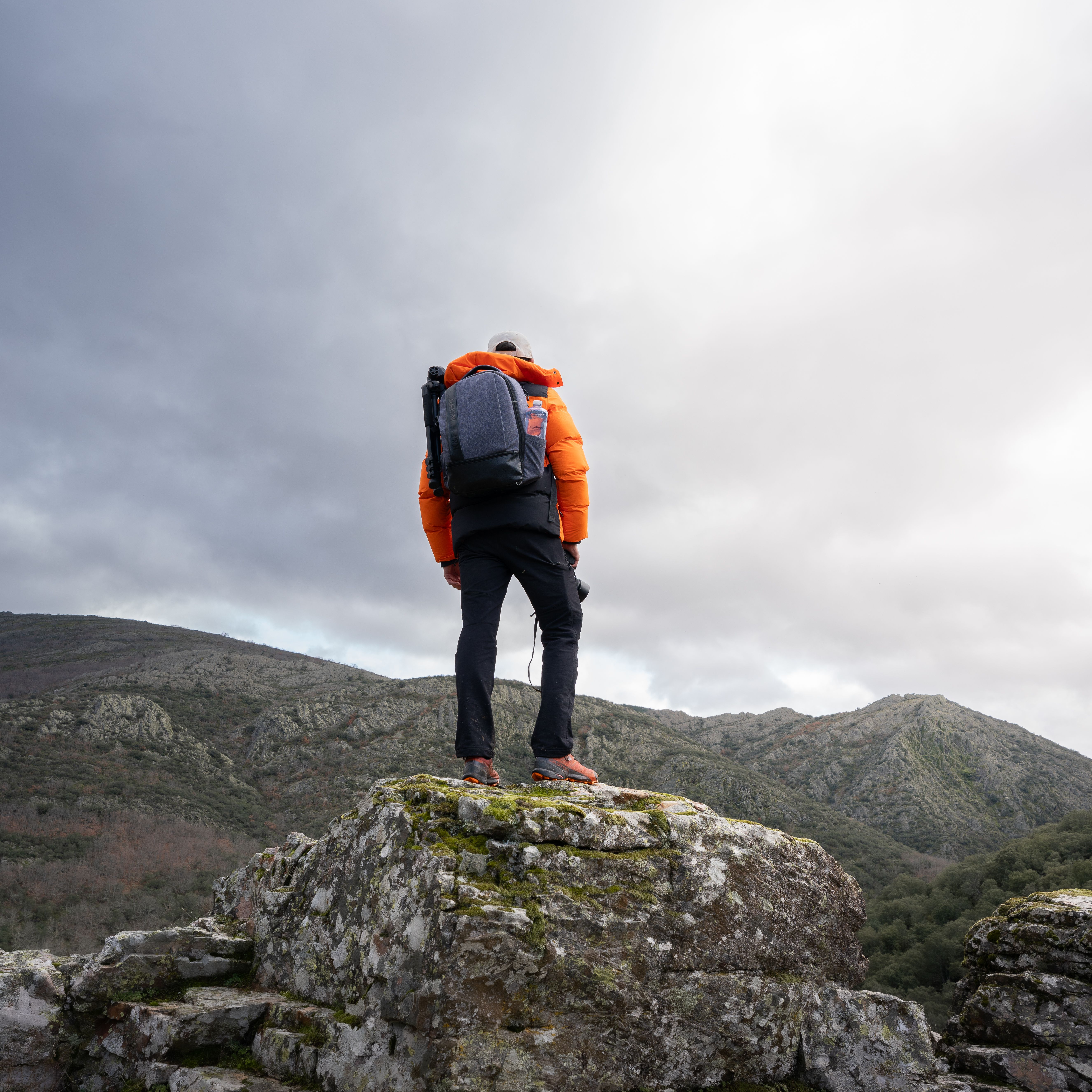 A lone hiker with a backpack stands on a rocky peak in Peñalba de la Sierra, Spain.