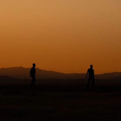 Free Silhouetted figures walking at sunset in a rural landscape, with a clear orange sky. Stock Photo