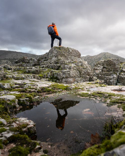 Man in Jacket and with Backpack Standing on Rocks