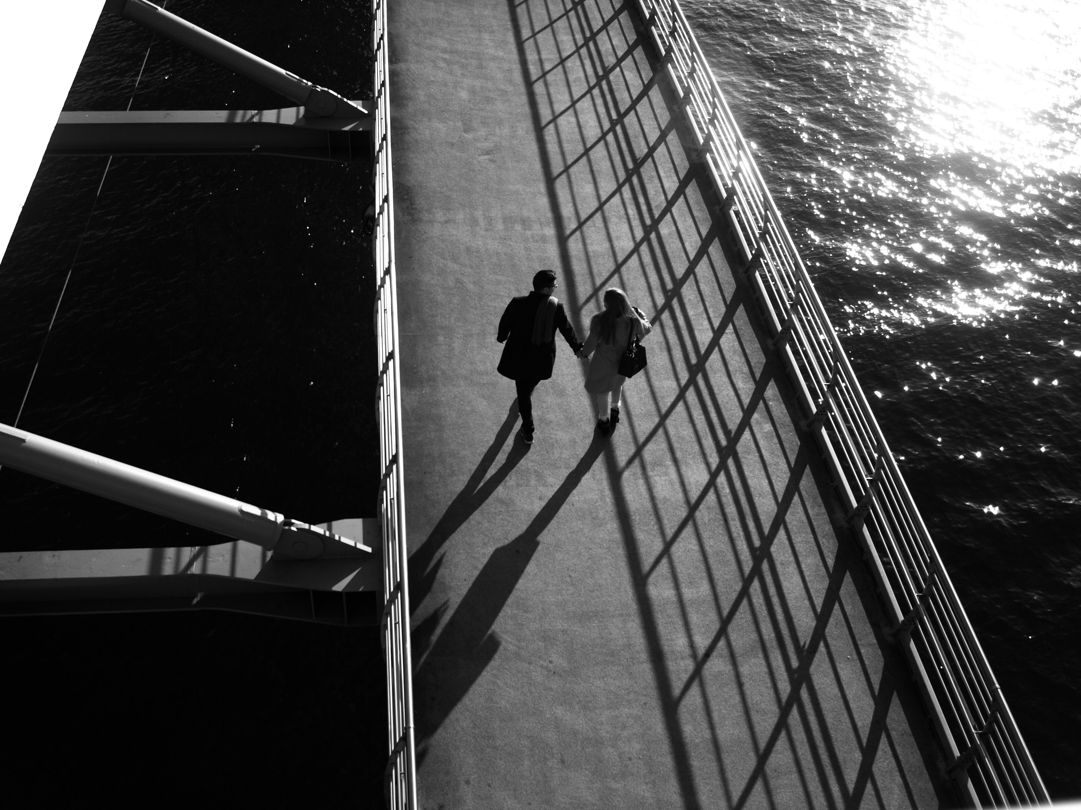 A black and white aerial shot of a couple holding hands on a bridge in Istanbul.