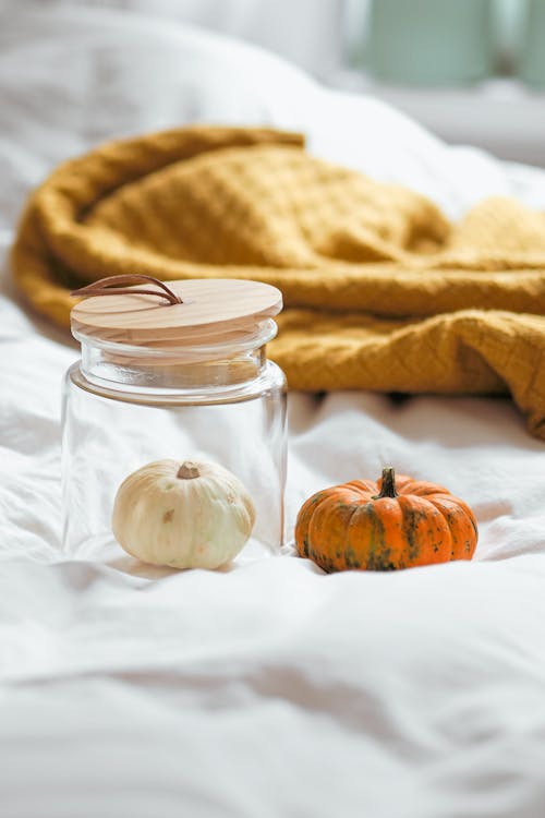 A jar with a pumpkin and a glass on a bed