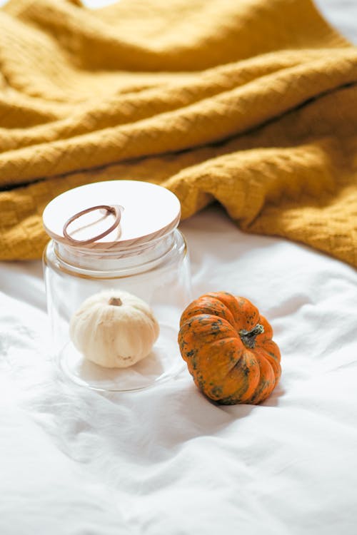 A jar with a pumpkin and a candle on a bed