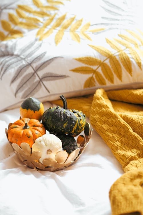 A basket filled with pumpkins and other fall decorations on a bed