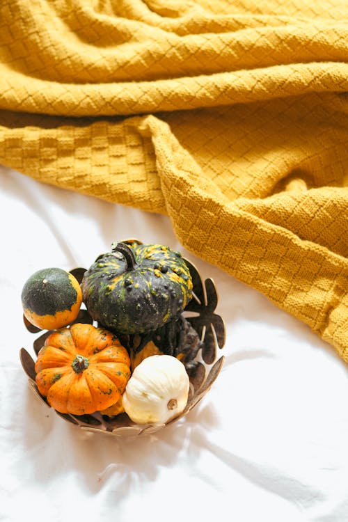 A basket filled with pumpkins and squash on a bed
