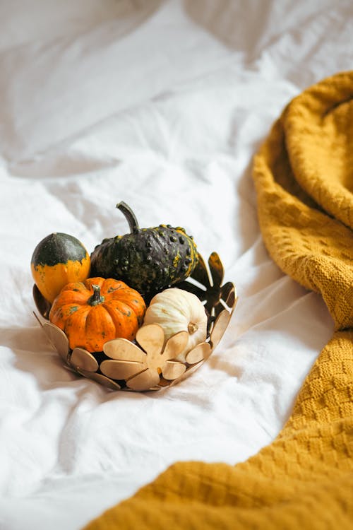 A basket filled with pumpkins and gourds on a bed