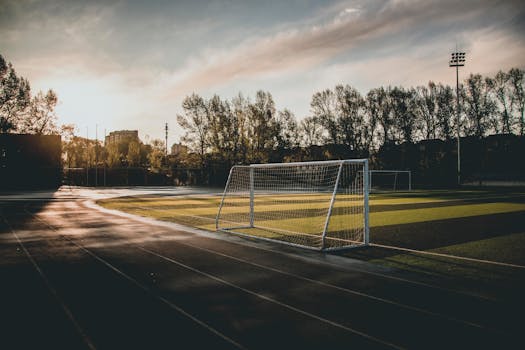 Beautiful view of an empty soccer field at sunset, with goalposts and dramatic sky.