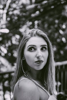 一张黑白特写肖像中，一位女子在户外优雅回眸，尽显美丽