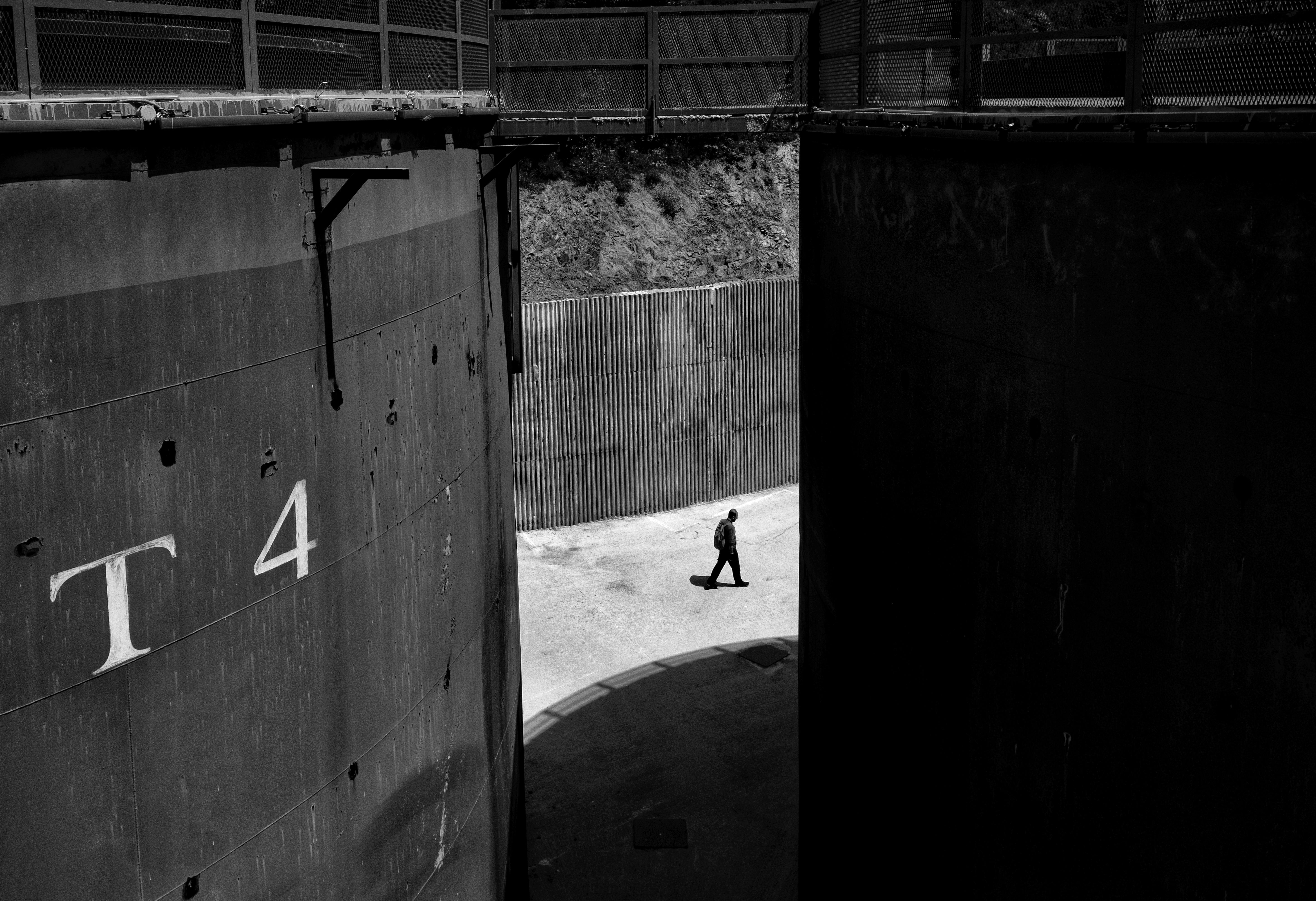A solitary figure walks through an industrial setting in a black and white photo capturing urban stillness.