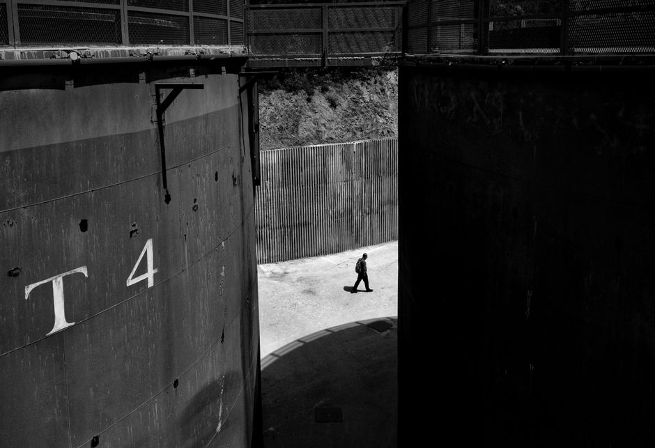 A solitary figure walks through an industrial setting in a black and white photo capturing urban stillness.