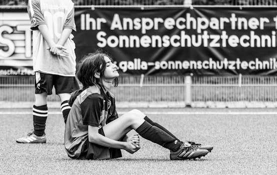 Young female soccer player sitting on a sports field in Germany.