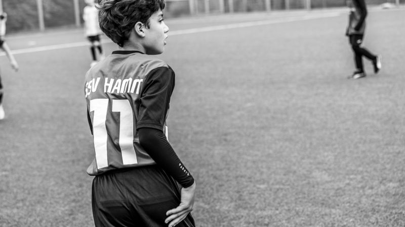 A young soccer player on a football pitch wearing a team jersey in Germany.