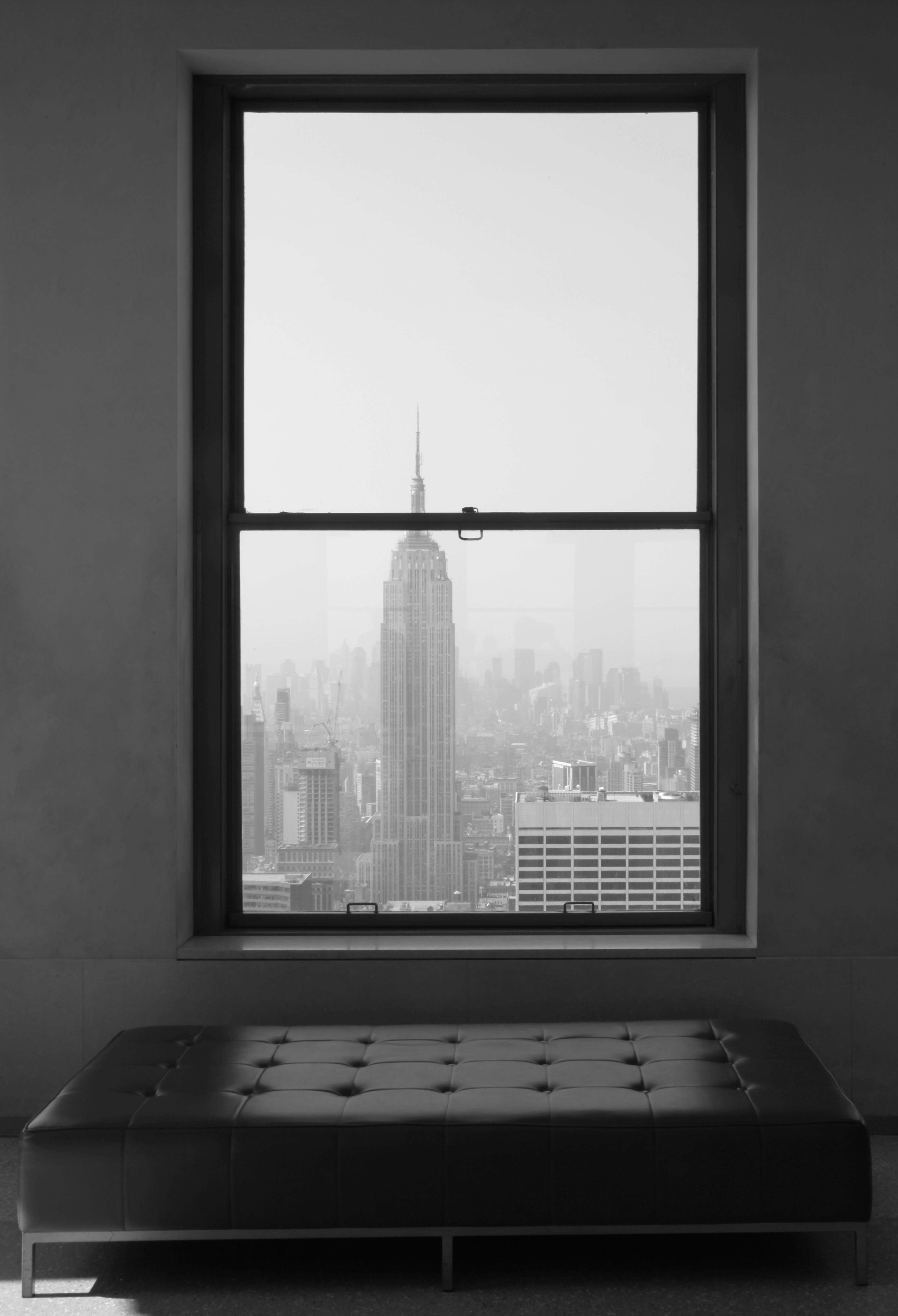 Black and white view of the Empire State Building from a room window in New York City.
