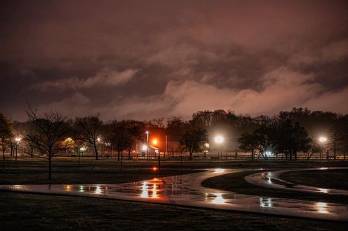 Free Captivating nighttime view of Stamford park lights reflecting on wet paths under dramatic clouds. Stock Photo