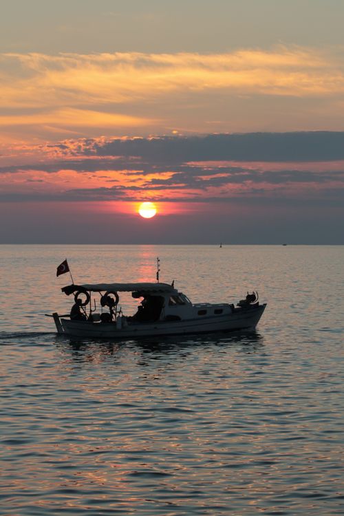 Free A tranquil sunset in Türkiye featuring a boat silhouette on the calm sea. Stock Photo