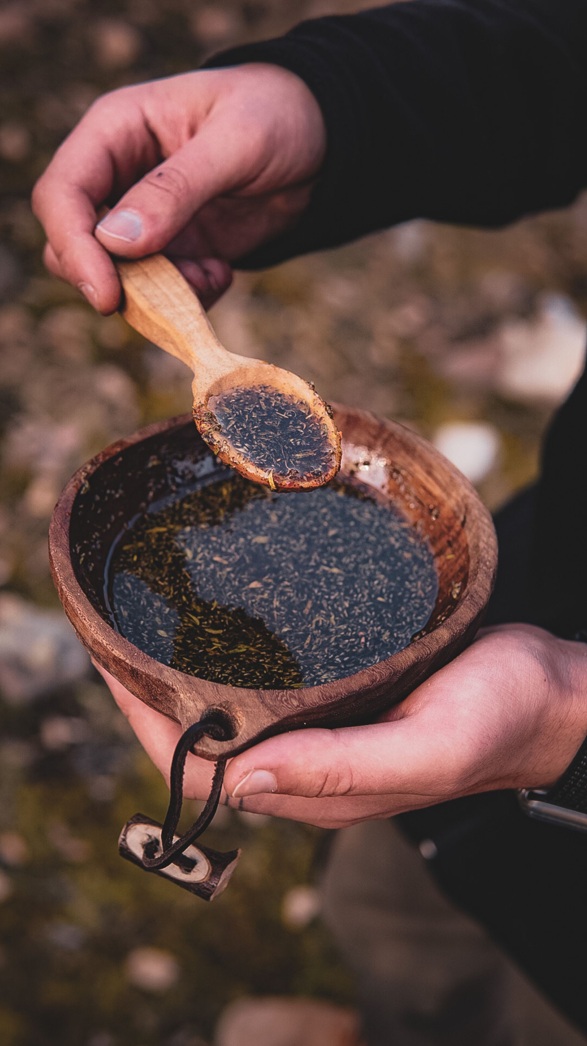 Hands holding a wooden bowl and spoon, filled with soup, capturing an outdoor rustic feel. - authentic shilajit